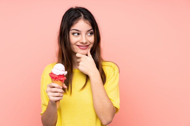 Joven mujer morena sosteniendo un helado de cucurucho rosa pensando en una idea y mirando de lado