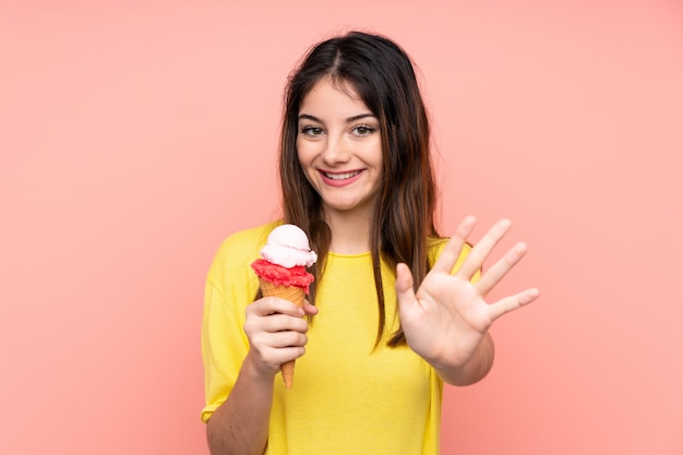 Joven mujer morena sosteniendo un helado de cucurucho rosa saludando con la mano con expresión feliz