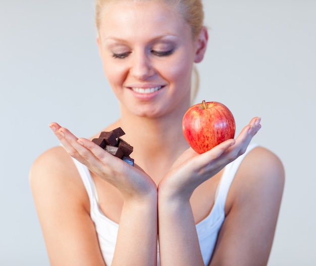 Joven mujer mostrando chocolate y manzana se centran en chocolate y manzana