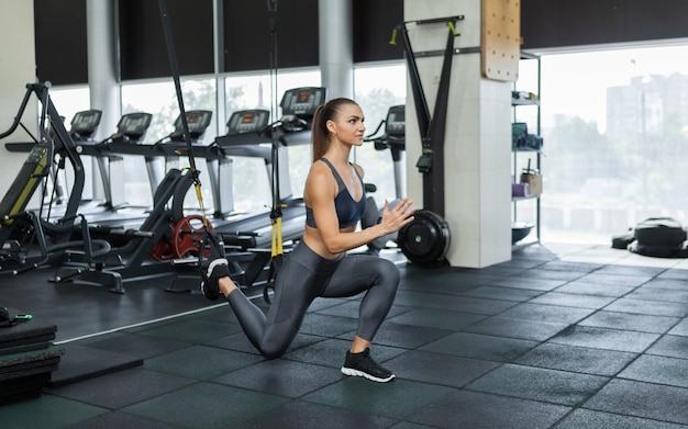 Joven mujer musculosa atractiva en ropa deportiva entrena músculos con sistema de resistencia trx en un gimnasio moderno. Entrenamiento cruzado. Aptitud moderna