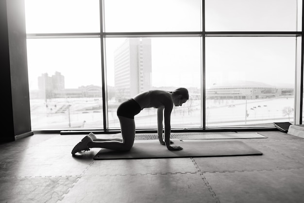 Joven mujer musculosa haciendo ejercicio básico en colchoneta de fitness en el gimnasio, haciendo flexiones en el club de salud.