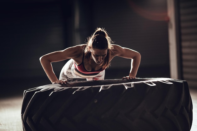 Joven mujer musculosa haciendo ejercicio push-up en un neumático en entrenamiento cruzado en el garaje.