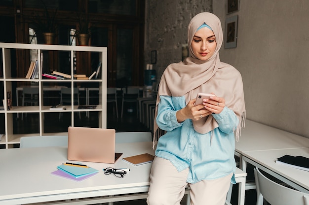 Joven mujer musulmana bastante moderna en hijab trabajando en la sala de la oficina, educación en línea