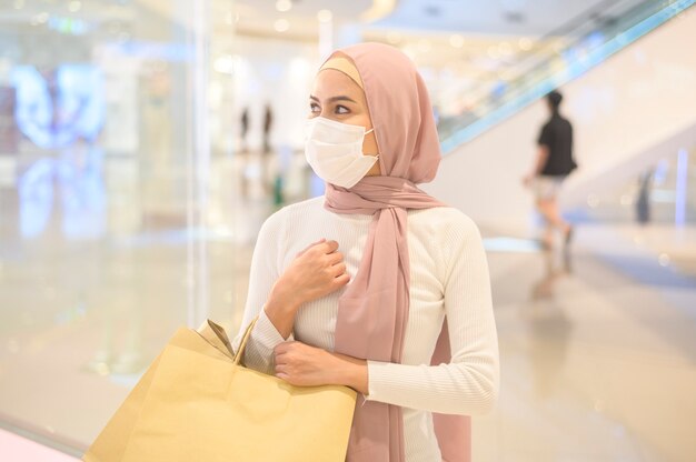 Una joven mujer musulmana con máscara protectora en el centro comercial