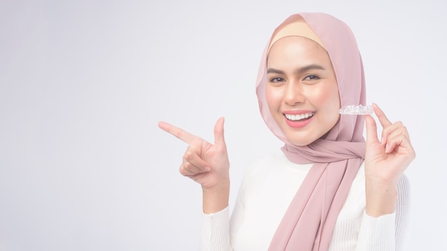 Una joven mujer musulmana sosteniendo aparatos invisalign en blanco, concepto de salud dental y ortodoncia.
