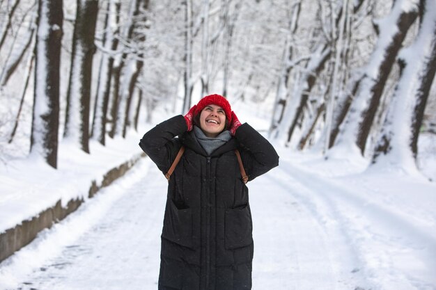 Joven mujer muy sonriente con abrigo de invierno con sombrero rojo en el parque forestal de la ciudad