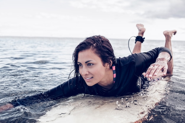 Joven mujer nadando sobre la tabla de surf en el agua