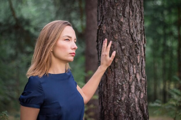 Joven mujer natural en vestido azul en el bosque Mano en tronco de pino con textura