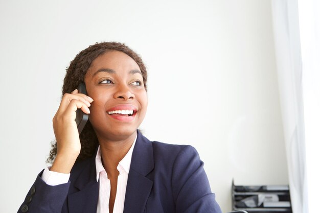 Joven mujer de negocios africana feliz en la oficina hablando por teléfono celular