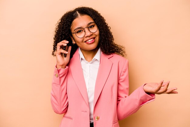 Joven mujer de negocios afroamericana sosteniendo un teléfono móvil aislado de fondo beige