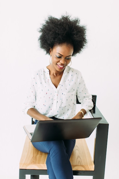 Joven mujer de negocios afroamericano escribiendo en la computadora portátil mientras está sentado en la silla, aislado en blanco