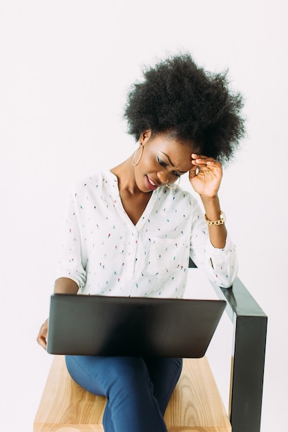 Joven mujer de negocios afroamericano escribiendo en la computadora portátil mientras está sentado en la silla, aislado en blanco