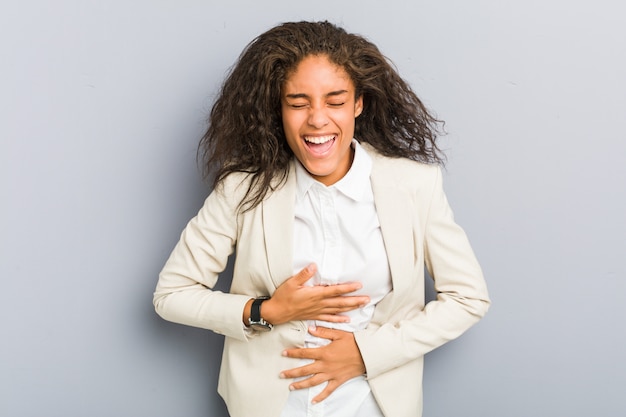 Joven mujer de negocios afroamericano se ríe alegremente y se divierte manteniendo las manos sobre el estómago.