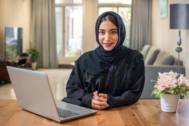 Joven mujer de negocios árabe con hijab y portátil en casa