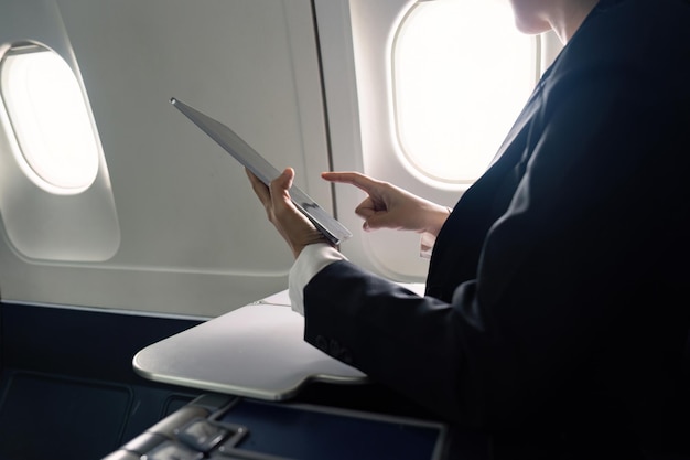 Una joven mujer de negocios asiática exitosa se sienta en la cabina de un avión y trabaja desde cualquier lugar volando en primera clase.