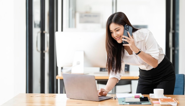 Joven mujer de negocios asiática hermosa encantadora sonriendo y hablando por teléfono móvil en la oficina