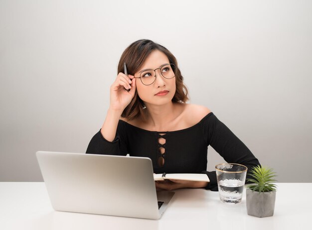 Joven mujer de negocios asiática pensando soñando sentada en el escritorio con una computadora portátil