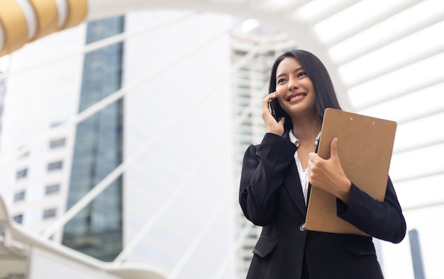 Joven mujer de negocios asiática profesional inteligente mediante teléfono móvil en la ciudad al aire libre