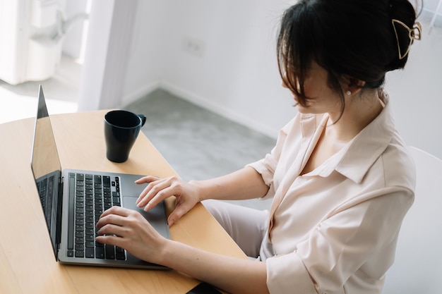 Joven mujer de negocios asiática sentada delante de una computadora portátil abierta leyendo el correo electrónico de un cliente