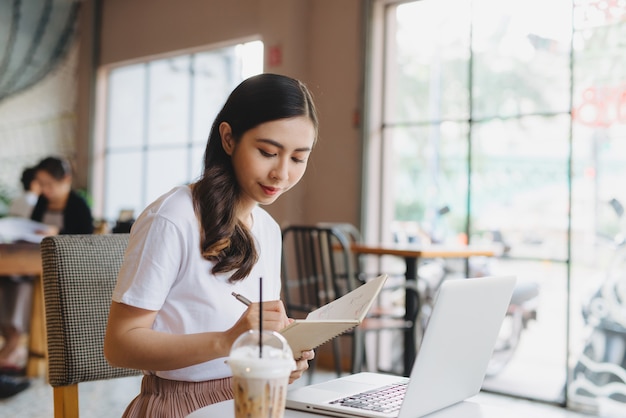 Una joven mujer de negocios atractiva sentada en un café con una computadora portátil y un café