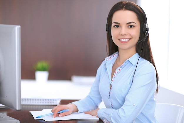 Foto joven mujer de negocios con auriculares, sentada en la mesa de la oficina.