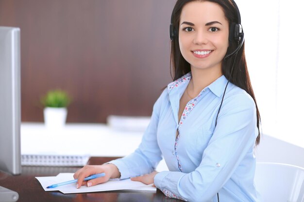 Joven mujer de negocios con auriculares, sentada en la mesa de la oficina.