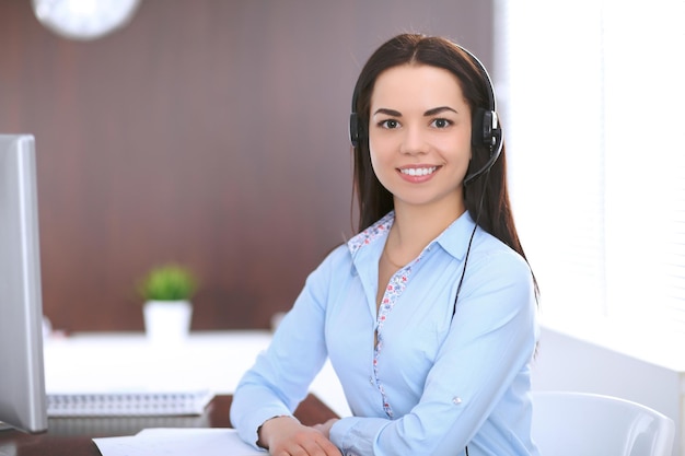 Joven mujer de negocios con auriculares, sentada en la mesa de la oficina.