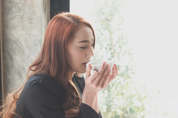 Joven mujer de negocios bebiendo café contra la ventana