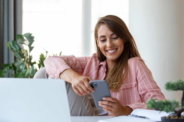 Una joven mujer de negocios bonita en la oficina sentada en una silla de oficina hablando en su teléfono inteligente