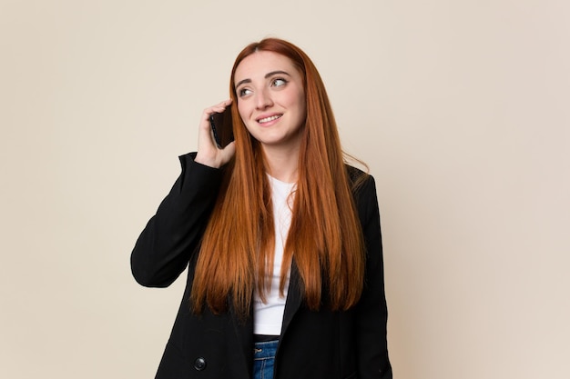 Joven mujer de negocios de cabello rojo usando su teléfono móvil aislado