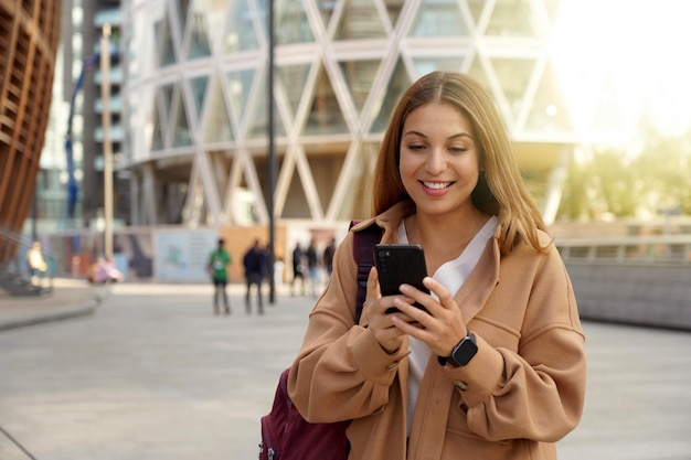 Joven mujer de negocios caminando en una ciudad moderna y sostenible usando un teléfono móvil