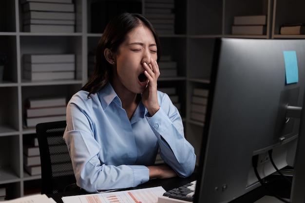 Una joven mujer de negocios cansada bostezando y sintiéndose somnolienta después de trabajar todo el día trabajando horas extras por la noche