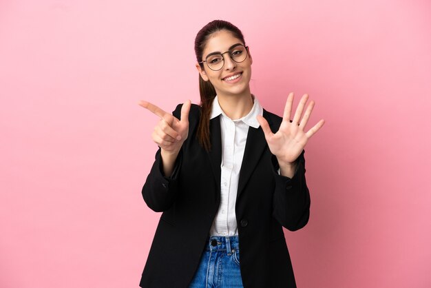 Joven mujer de negocios caucásica aislada sobre fondo rosa contando siete con los dedos