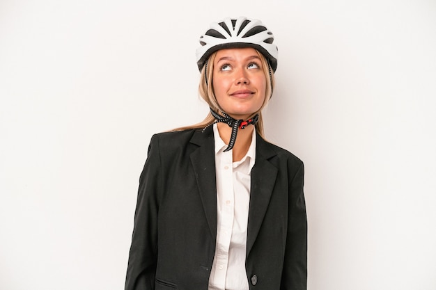 Joven mujer de negocios caucásica con un casco de bicicleta aislado sobre fondo blanco soñando con lograr metas y propósitos