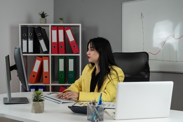 Joven mujer de negocios caucásica trabajando con computadora portátil y gráficos y gráficos financieros