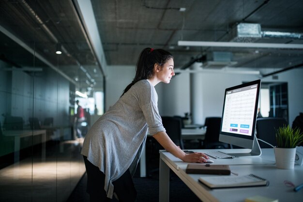 Joven mujer de negocios con computadora de pie en una oficina trabajando