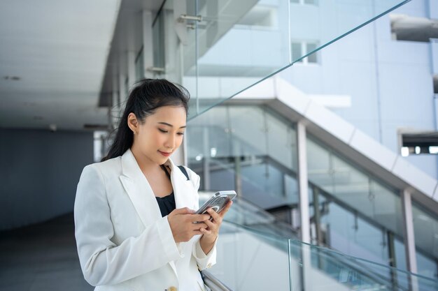 Foto joven mujer de negocios con un documento y usando un teléfono inteligente mientras camina por la ciudad