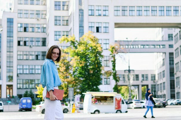 joven mujer de negocios elegante en anteojos, ropa casual. caminando. calle de la ciudad hablando por telefono