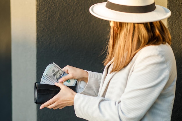 Joven mujer de negocios esconde dólares estadounidenses en una billetera negra cerca de manos femeninas El concepto de ahorro de pagos en efectivo