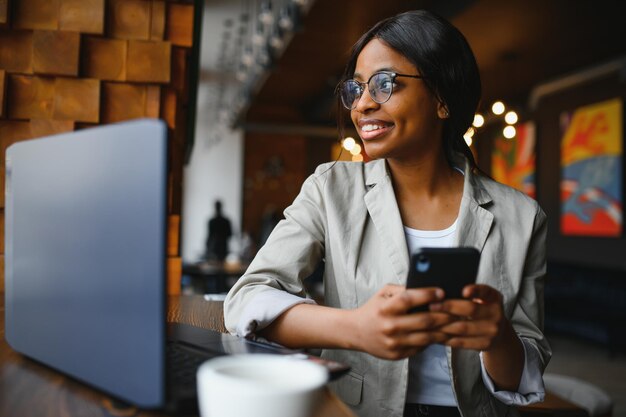 Una joven mujer de negocios está organizando la próxima reunión de negocios en un moderno espacio de coworking usando una computadora portátil Una joven mujer independiente está leyendo correos electrónicos y otros mensajes en un teléfono móvil