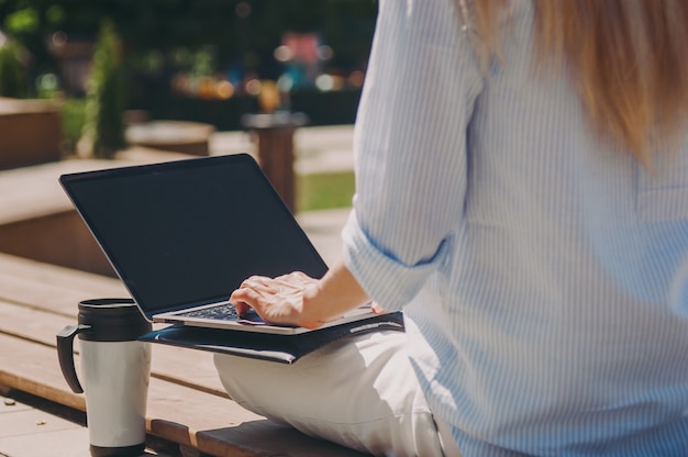 Una joven mujer de negocios está trabajando con una computadora portátil con una camisa azul en la calle en un parque