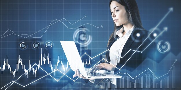 Joven mujer de negocios europea atractiva que usa una computadora portátil con una cuadrícula de gráficos de negocios brillante en un fondo borroso de la ciudad Concepto de finanzas y tecnología Doble exposición