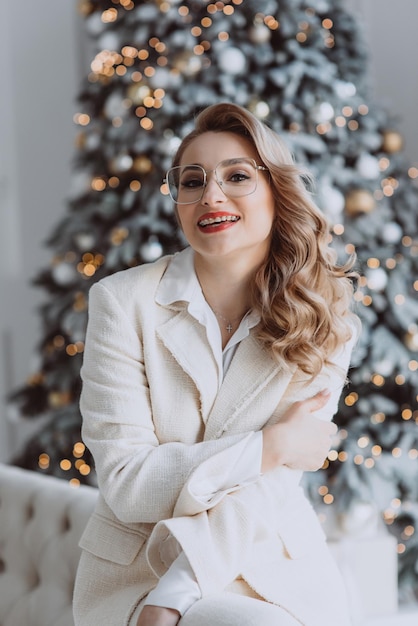 Joven mujer de negocios europea feliz con gafas sentada en el lugar de trabajo con un árbol de Navidad decorado detrás de una mujer sonriente que trabaja en la oficina en casa durante las vacaciones de invierno Enfoque selectivo suave