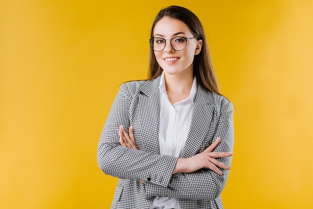 Una joven mujer de negocios feliz con chaqueta y camisa con gafas sonríe y posa en la cámara con fondo amarillo