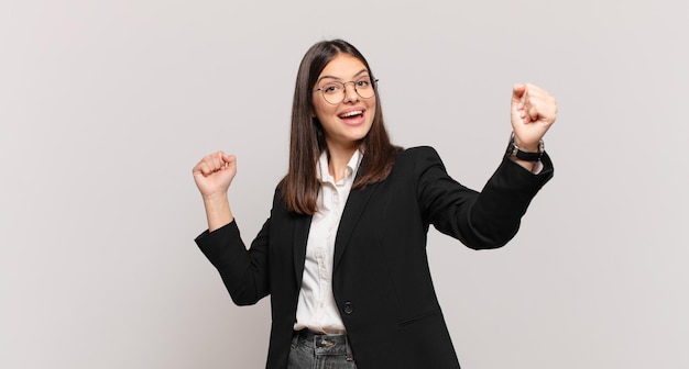 Joven mujer de negocios gritando triunfalmente, luciendo como una ganadora emocionada, feliz y sorprendida, celebrando