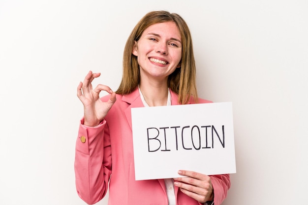 Joven mujer de negocios inglesa sosteniendo un cartel de bitcoin aislado de fondo blanco alegre y segura mostrando un gesto correcto