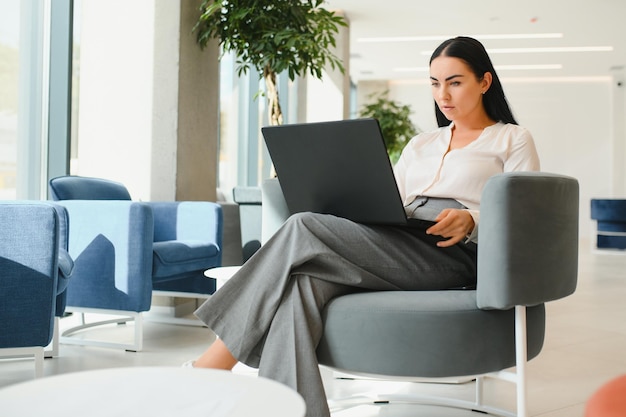 Joven mujer de negocios con laptop sentada en el vestíbulo del centro de negocios