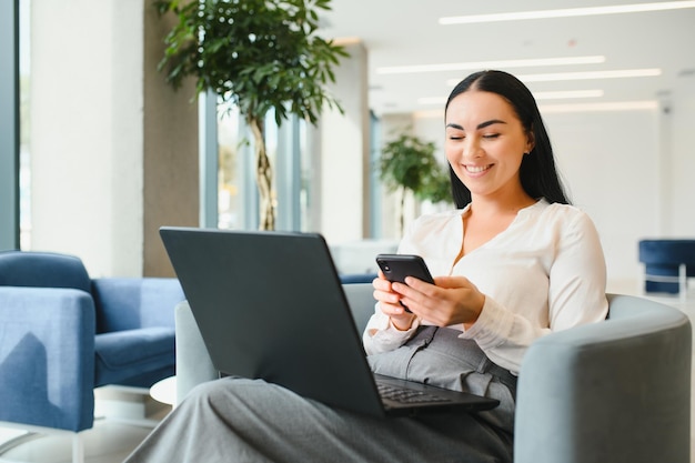 Joven mujer de negocios con laptop sentada en el vestíbulo del centro de negocios