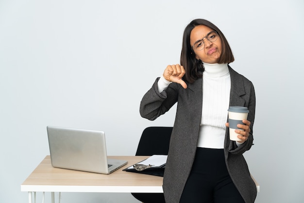 Joven mujer de negocios latina que trabaja en una oficina aislada sobre fondo blanco mostrando el pulgar hacia abajo con las dos manos