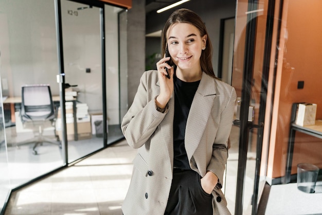 Joven mujer de negocios en una llamada telefónica caminando por los corredores de la oficina equilibrada y dinámica